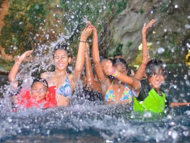 A group of people laughing under a burst of water on a river stop
