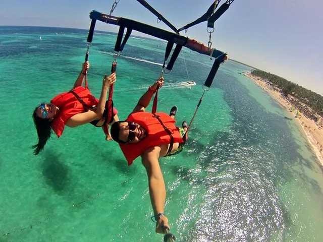 Two people harnessed under a parasail above shallow turquoise water