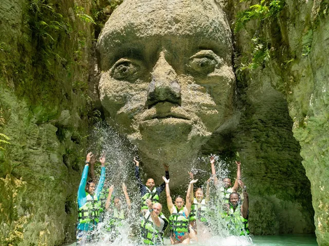 A group in life jackets under a carved stone face in a river canyon